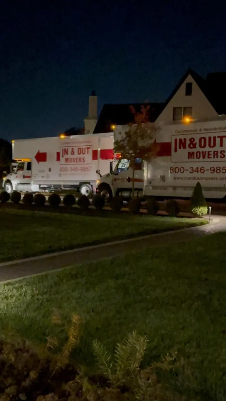 Two In & Out Movers trucks parked outside a residential home at night during a move-in or move-out service.