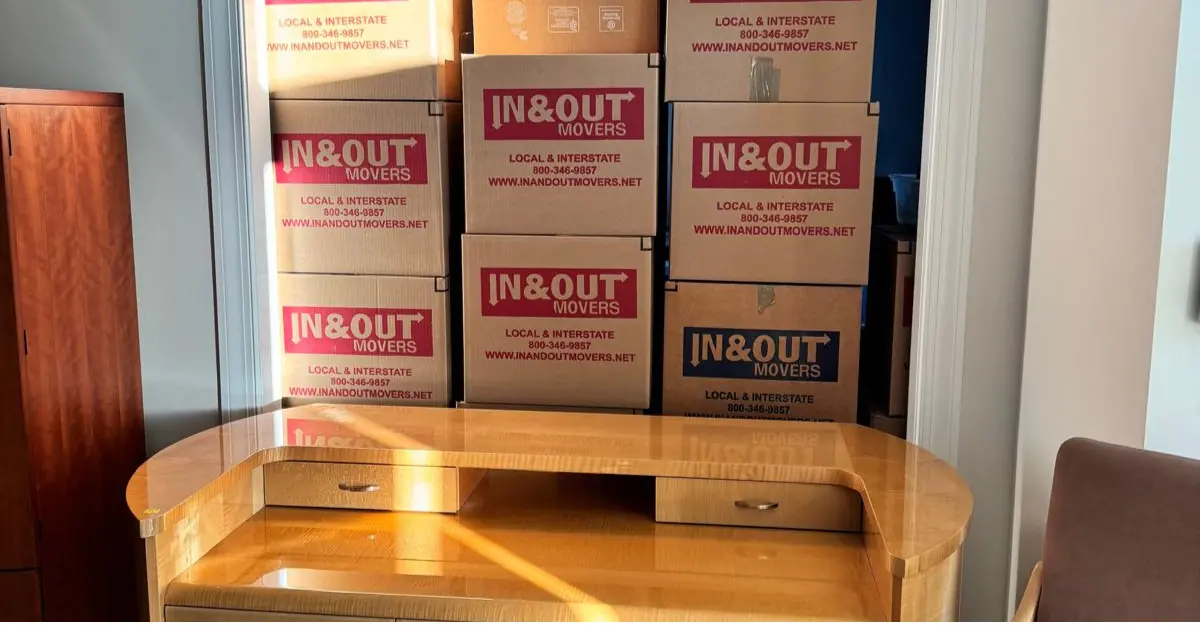 Stacked In & Out Movers boxes behind a wooden desk in a home interior, ready for packing for small international moves.