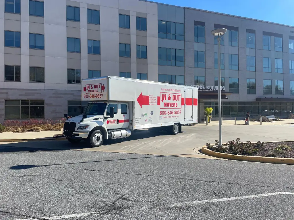 In & Out Movers truck parked outside a large office building under clear daylight