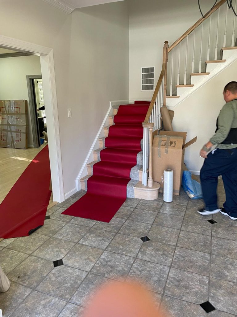 Red protective runner covers a staircase and hallway while movers pack for a move inside a residential home.