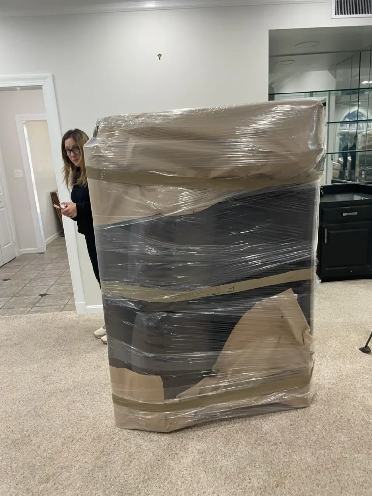 Large furniture piece wrapped for moving with a woman nearby during partial packing preparations.