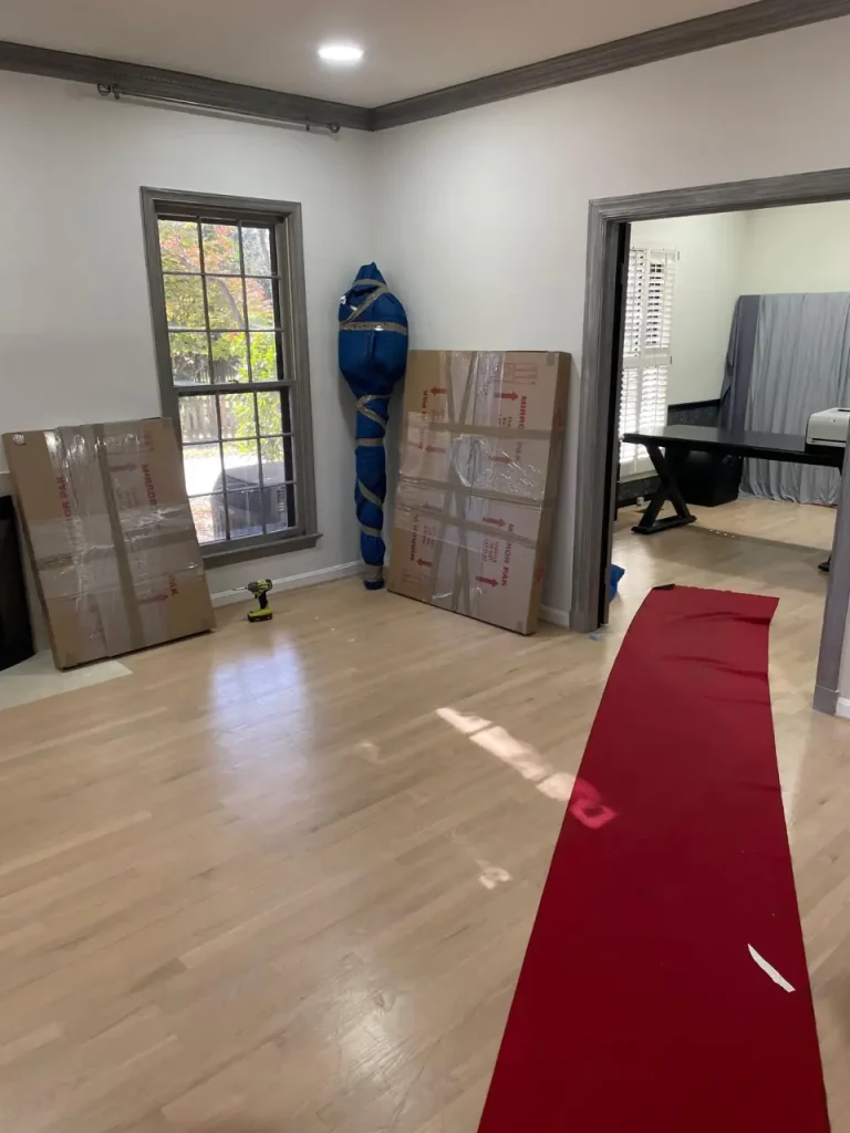 Packed boxes and wrapped furniture in an empty room with hardwood floors during small international moves preparation.